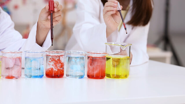 Children in Lab Coats Using Droppers for Science Experiment