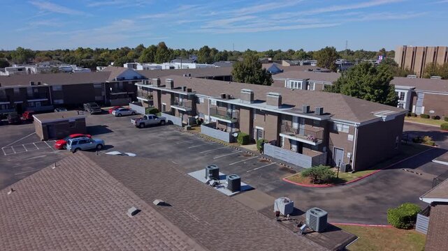 Sunny daytime aerial view of a residential neighborhood with rows of multifamily housing buildings and organized parking.
