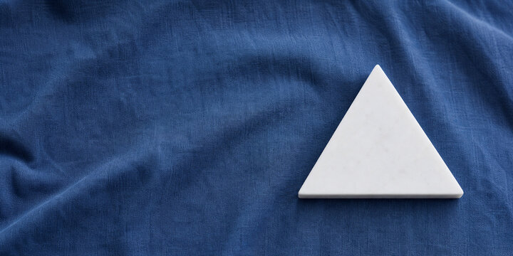 equilateral. Single white equilateral triangle object on deep blue linen, calm still life for editorial concept, lifestyle magazines.