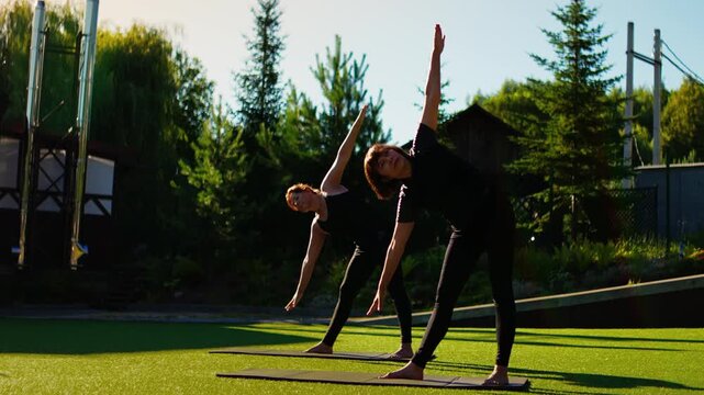 Elderly women practicing outdoor Pilates in slow motion, performing standing stretches and balance poses together on yoga mats in a peaceful green garden setting