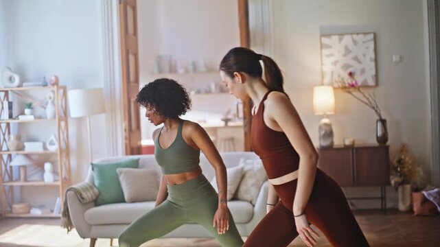 Diverse friends practicing warrior yoga pose home living room. Wellness workout.