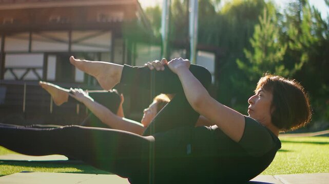 Elderly women practicing gentle Pilates exercises outdoors on yoga mats, stretching legs and strengthening core muscles together in serene slow-motion fitness routine