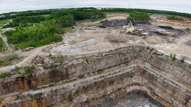 Sweeping drone view across layered quarry terraces and exposed gray rock near a wooded horizon