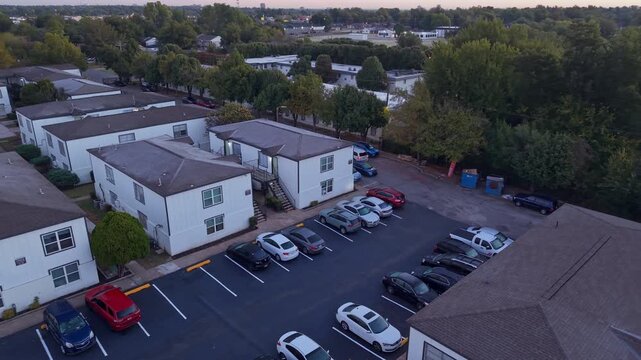Evening aerial view of a multifamily housing complex with residents returning home and parked cars filling the lot.