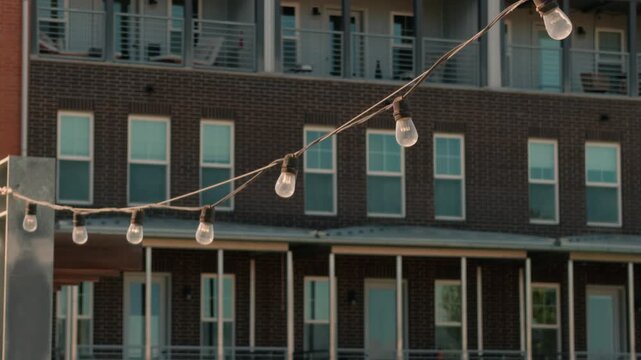 Static shot focused on hanging bulbs above an apartment patio gathering area.