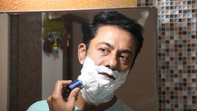 Middle-aged man shaving in front of a bathroom mirror during his daily grooming routine at home.