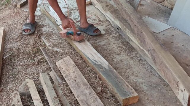 Commercial stock video showing a craftsman's hands operating an electric planer machine over a rough wood plank in a workshop.