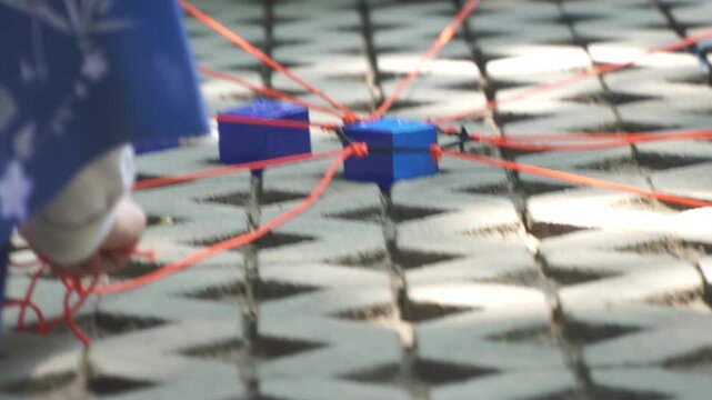 Group of people playing a teamwork game using orange ropes to lift a blue cube together, representing corporate collaboration, problem solving, leadership, and outbound teambuilding activity.