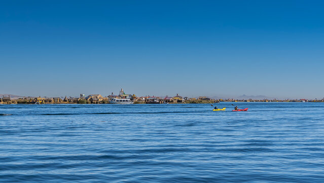 Tourist canoes float on the blue lake. Reed huts are visible on the far shore. The reed boats balsa de totora are moored. Peru. Lake Titicaca. Uros Floating Islands. Copy space.