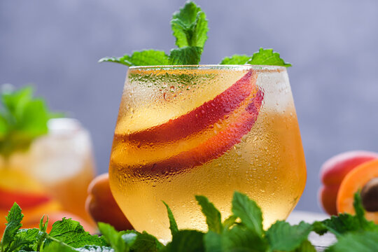 Cold summer beverage with sliced fresh nectarines, mint leaves, and ice in a condensed glass, garnished with fresh mint and fruit on a textured tabletop.