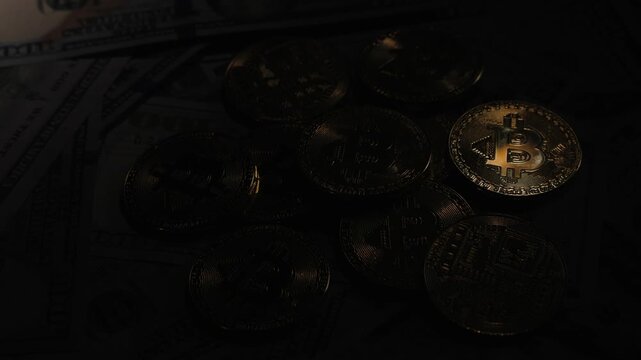 Shiny gold bitcoins are appearing and disappearing from dark background to light background revealing hundreds of american dollar bills, demonstrating the concept of cryptocurrency growth and fall in