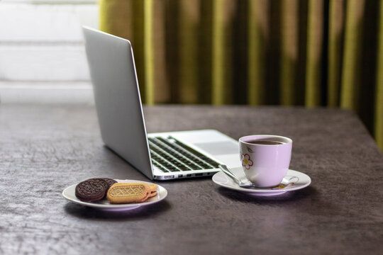 Open laptop computer on a table with a cup of hot chocolate and a plate of cookies