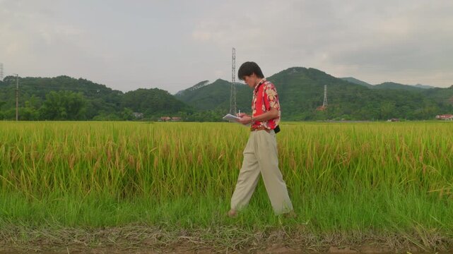 Young man walking beside a rural field while writing in a notebook, drawing inspiration from nature. Ideal for themes of creativity, storytelling, songwriting, journaling, and artistic process