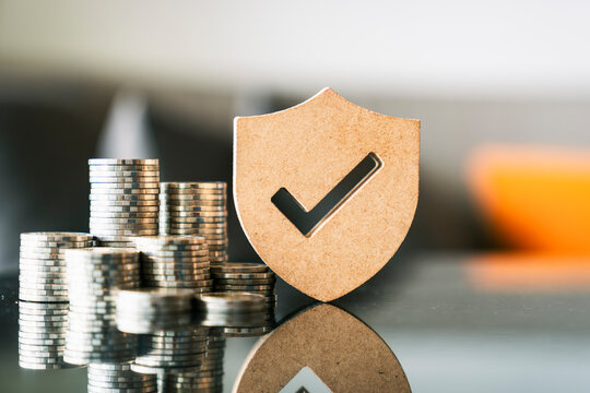 Financial security, wealth protection and money insurance concept. Wooden shield with check mark and coin stack. Ideal for banking, secure investment, savings, and economic growth business.