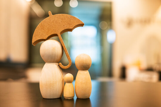 Family life insurance, social security and property protection concept. Wooden figures under umbrella. Ideal for healthcare planning, child welfare, safety, and home insurance business.