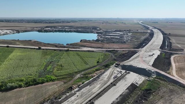 Drone aerial view of construction truck driving on partially built road. Highway infrastructure project with earthworks, soil compaction and gravel transport for modern civil engineering 