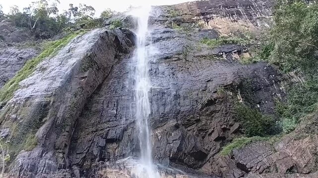 Horizontal view of high cliff section of Diyaluma waterfall in Sri Lanka showing strong winds scattering cascading water into fine mist spray