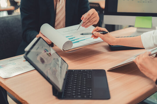 Business colleagues discussing financial charts and marketing data on tablet in office.