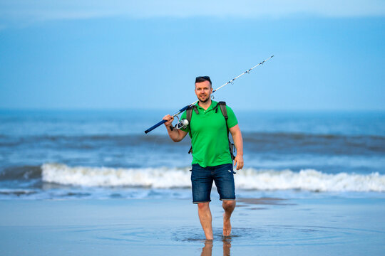 Fishing man walks near ocean water. Fishing rod and reel in hand. Fishing on shoreline with surf waves. Fishing lifestyle shows outdoor recreation.