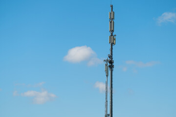 Obraz premium Tall cell tower stands against a clear blue sky with scattered clouds on a sunny day in a suburban area