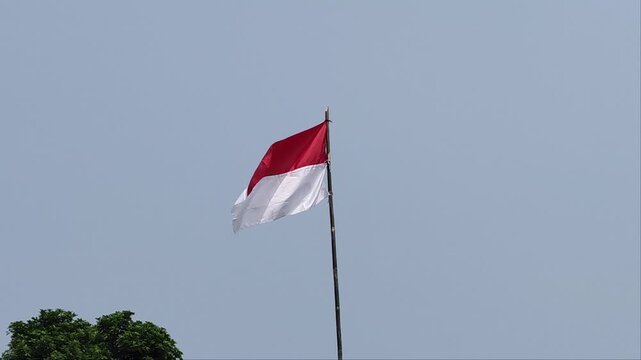Indonesian national flag waving on a traditional bamboo pole against a clear blue sky