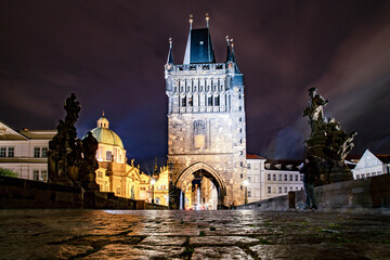 Obraz premium Old Town Bridge Tower on Charles Bridge at Night in Prague. Night Old Town Bridge Tower on Charles Bridge in Prague. Prague Gothic architecture. Baroque historic dome of St. Francis of Assisi Church.