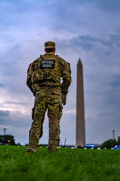 National Guard stands near Washington Monument. Armed Guard patrols public event. American National Guard protects national capital. National Guard soldier watches evening security.