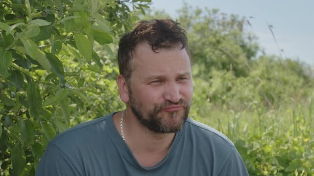 Medium shot portrait of the young adult caucasian man talking something on the camera with natural green background