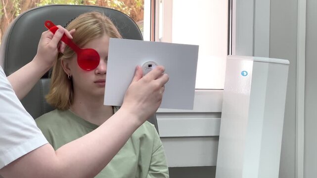 Optometrist examining a young girl vision with test charts and trial frames. eye clinic checkup, pediatric ophthalmology exam, medical care.