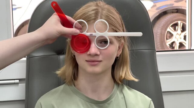 Doctor testing a young girl vision with trial frames in an eye clinic. optometry examination, pediatric eye care, medical consultation.