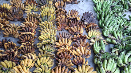 Obraz premium A top view of assorted banana bunches arranged on a tarp at a traditional market, showcasing different stages of ripeness from green to yellow and brown