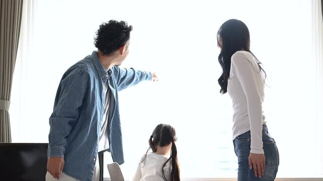 旅行先のホテルで窓の外の景色を眺める30代の日本人夫婦と6歳の子どもの後ろ姿