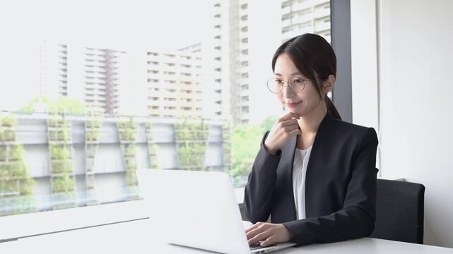 ノートパソコンを使って仕事をする眼鏡姿の20代日本人女性