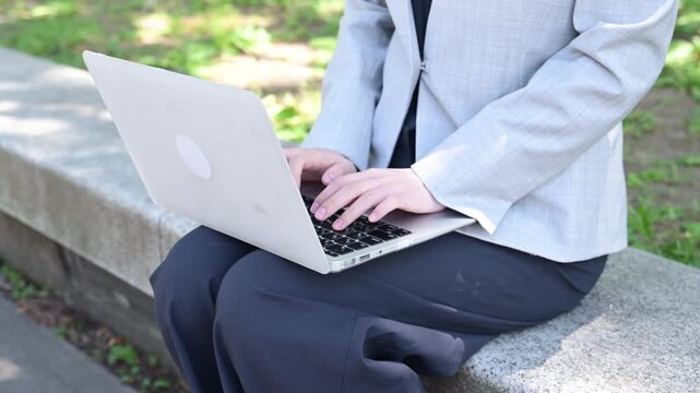 公園のベンチでノートパソコンを操作する20代日本人ビジネスウーマンの手元
