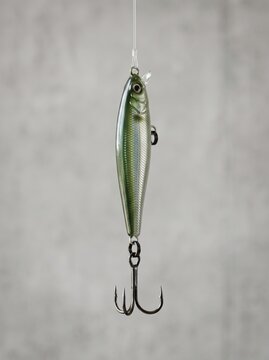 Green metallic fishing lure suspended vertically against neutral grey studio background with hanging vertically thin line against plain