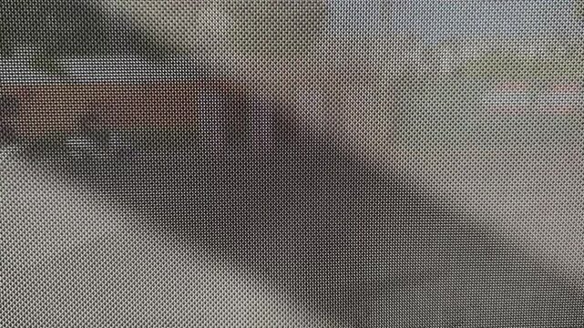 Close-up texture of a sun shade or fine mesh screen grid with dark diagonal shadows and blurry motorcycle background