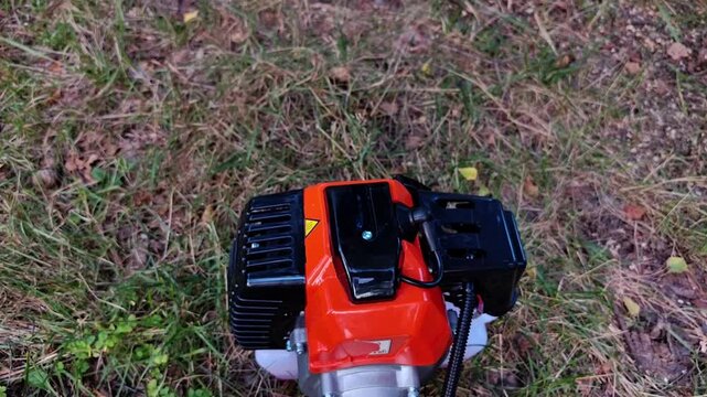 Man pulls the recoil starter to start a gasoline brush cutter engine on grass, garden equipment operation, landscaping work, outdoor maintenance, summer season