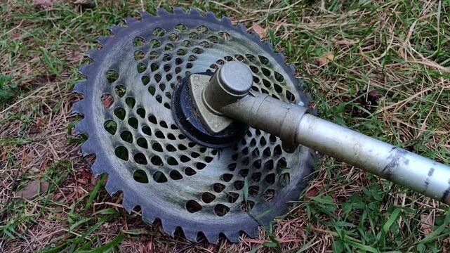Close up of a brush cutter metal cutting blade on grass, landscaping equipment, garden maintenance, outdoor machinery, summer season.