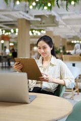 Fototapeta premium Young Asian Woman Reviewing Documents on Clipboard at Modern Co working Space with Laptop