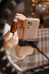 Fototapeta na wymiar Beauty blogger promoting facial serum during live streaming with smartphone and ring light. Skincare, beauty influencer, cosmetic review and healthy skin