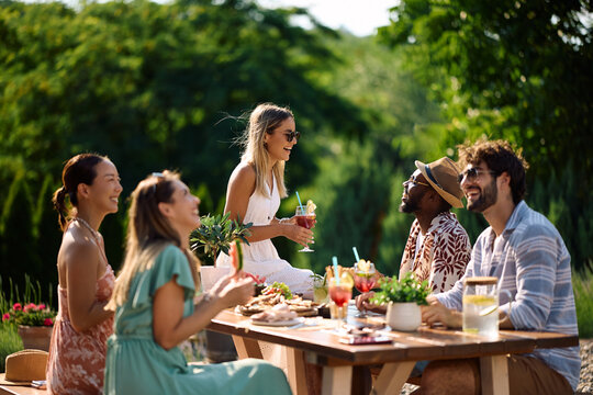 Happy woman talking to her friends while hosting summer party in her backyard.