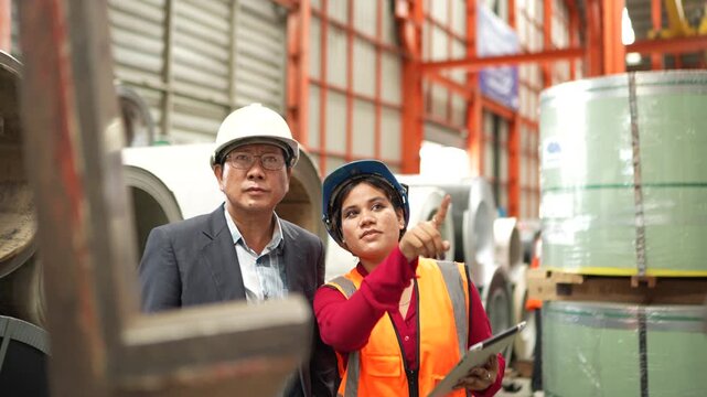 Industrial inspection team checking steel coil inventory and quality records in manufacturing warehouse. Material verification, factory operations and production management.
