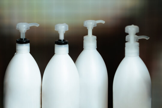 White Plastic Pump Bottles With Professional Products In Hair Salon. Row of cosmetic dispenser containers filled with shampoo or lotion on hair stylist workstation shelf
