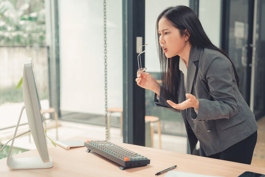 Stressed Asian businesswoman holding hand on forehead looking at computer screen with worried expression.