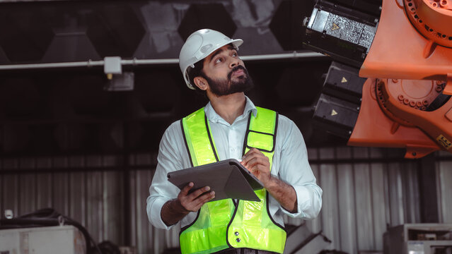 Professional technician observing robotic equipment while recording production status and inspection results inside an automated manufacturing facility