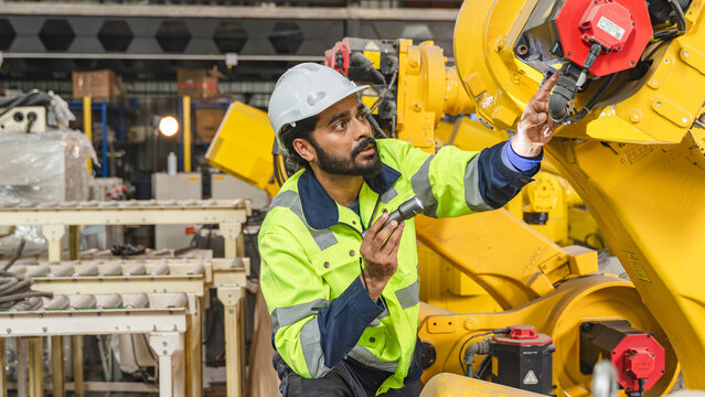 Professional engineer examining the robot end effector while carrying out preventive maintenance and equipment inspection inside an industrial production facility.