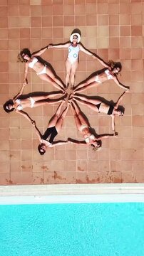 Top-down aerial view of a group of female friends in swimwear lying by the pool, holding hands, and creating a beautiful star figure, symbolizing unity, teamwork, and a luxury summer vacation