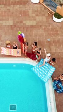 Aerial view of a group of cheerful young women in bikinis with colorful inflatable floats, celebrating and having fun together at a luxury resort swimming pool party during summer vacation