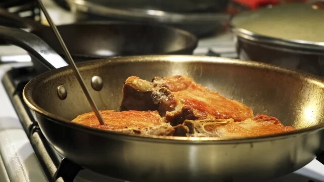 Cooking pork meat in a steel pan on a kitchen stove, close-up side view. Measuring the temperature of meat using a heat probe.
