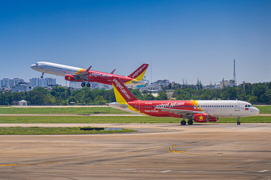 Commercial aircraft taking off with airport apron vehicles and wing view at Tan Son Nhat Airport, Vietnam